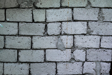 Obraz premium A wall of gray concrete blocks bonded with cement with large gaps. The surface is uneven and rough, with exposed cement mortar.