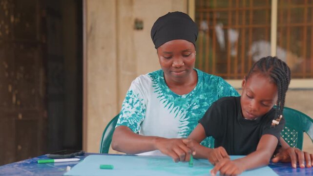 African mother teaching daughter craft at table, outdoor veranda classroom feel, black mother wearing headwrap instructing schoolage daughter in clay modeling, handson activity, focused concentration,