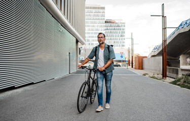 Man pushing his bike by his side, walking down the street. © Halfpoint