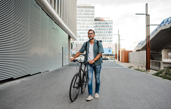 Man pushing his bike by his side, walking down the street.