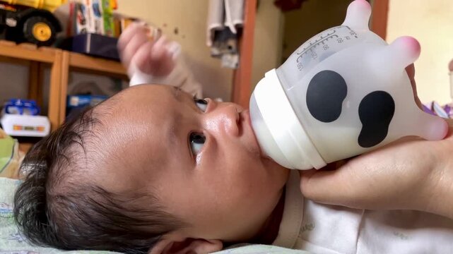 cute newborn baby drinking milk from a bottle with a cow pattern at home