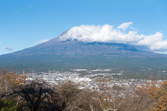 A scenic panoramic view of snow-capped Mount Fuji overlooking Fujinomiya city from Shirao Mountain Park (Shiraosan) in Japan, during a sunny December afternoon.