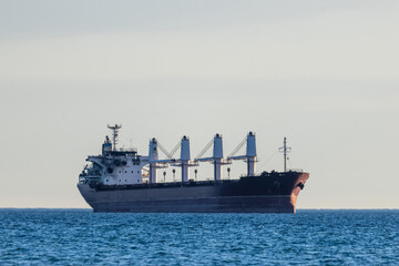 A large cargo ship with deck cranes with a damaged wheelhouse as a result of a drone attack, standing on calm open water, side view © Andrey Solovev