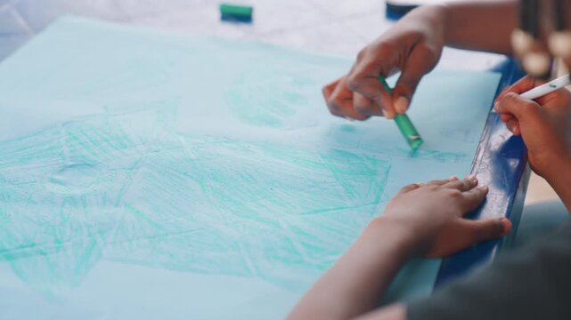 Black child drawing while mother guides hand, overhead view of braided child and adult hands shaping lines with green crayon and eraser, intimate learning moment, focused instruction and tactile