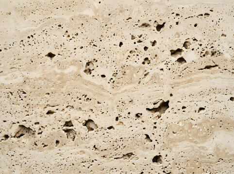 Macro texture of warm beige travertine stone with deep irregular porous cavities and layered sedimentary striations