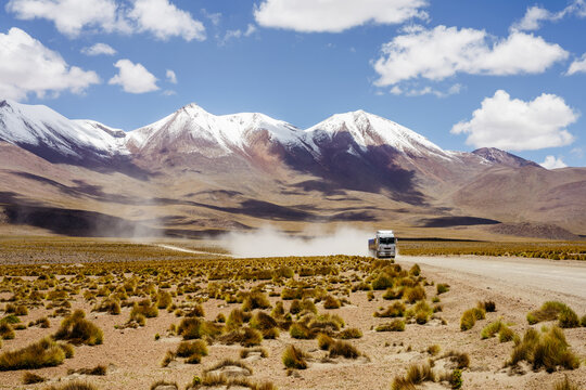Truck raising dust below snow-capped mountains on the altiplano, Sud L&iacute;pez, Potos&iacute;, Bolivia