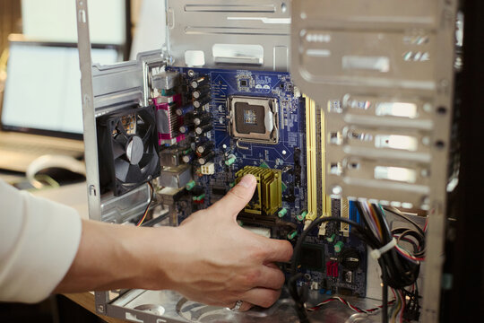 Asian male technician hand installing hardware component inside open computer tower, upgrading system motherboard. Image suitable for IT support and hardware repair services