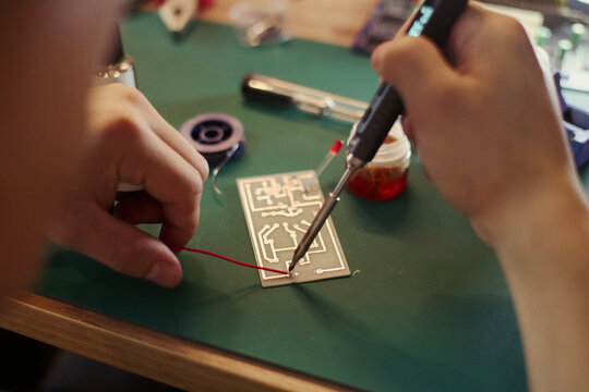 Hands of young Asian male soldering wire to circuit board, focusing on engineering and electronics assembly. Ideal for STEM education and hardware development marketing, close up