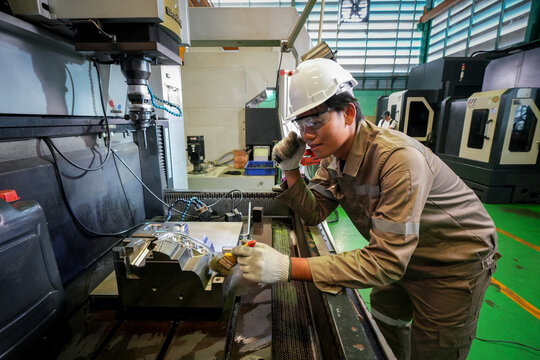 Machining factory technician maintenance inspection safety helmet safety glasses metalworking, worker checking milling equipment with flashlight in industrial workshop, focused quality control