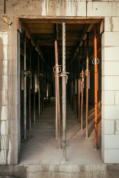 View through a block doorway of adjustable metal shoring jacks holding up a wooden ceiling structure on a construction site.