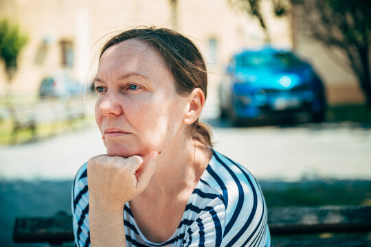 Middle-aged woman sitting on a park bench with a thoughtful expression. Reflection, contemplation and peaceful urban lifestyle concept.