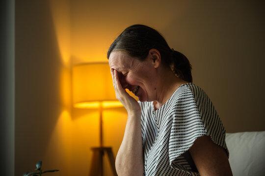 Middle-aged woman smiling and laughing in her living room after recalling a happy memory. Optimism, relief and everyday lifestyle theme.