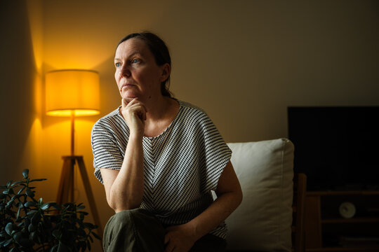 Mature woman looking out the window with a serious expression. Reflection, uncertainty and thoughtful decision-making concept.