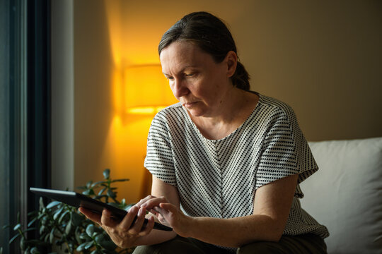 Woman using a tablet computer in a comfortable home setting during the evening. Digital lifestyle, remote work and online communication concept.