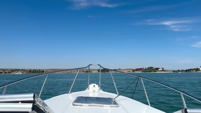 View from the front of a motorboat cruising across calm blue water on a bright summer day. The boat moves toward an open horizon, creating a strong sense of freedom, travel and leisure. 
