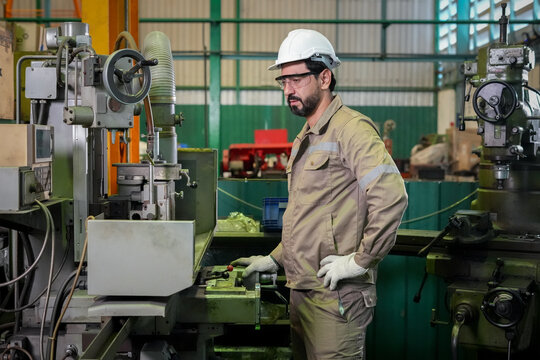 Industrial worker machinist factory machine metal manufacturing safety helmet glove, focused man operates milling equipment inside workshop with protective eyewear and workwear, production concept