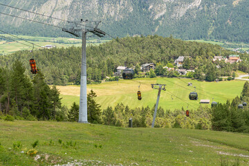 Imst, Austria. Cable cars crossing a forested Alpine valley above green meadows and mountain villages © Dirk