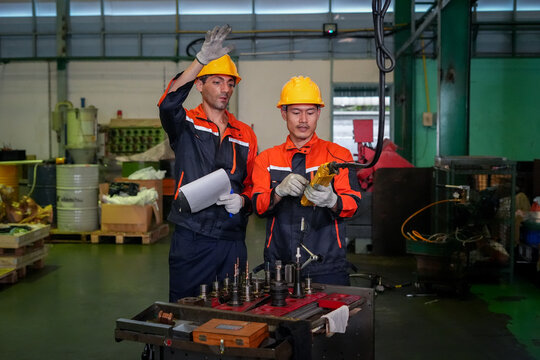 Factory worker engineer helmet safety machine maintenance inspection teamwork during equipment check on industrial workshop floor, focused male staff reviewing checklist and tool setup