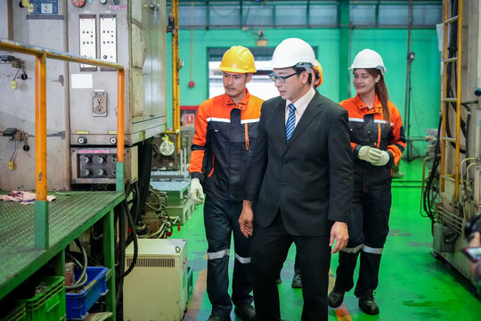 Factory industrial engineer manager inspection safety machinery helmet business suit walking with worker in coverall inside manufacturing plant, audit promoting compliance culture