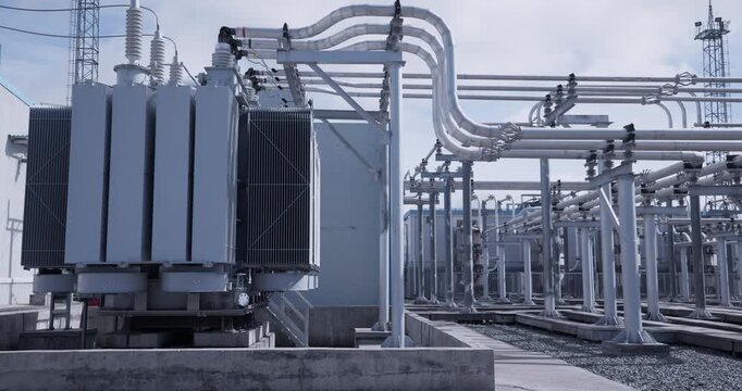 Large power transformers and bus piping at outdoor electrical substation with utility towers and concrete platforms.