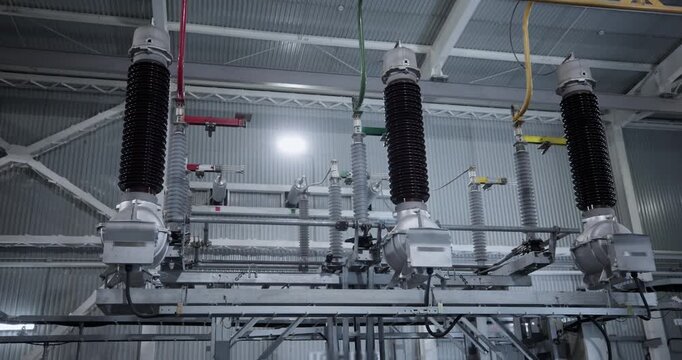 Electrical substation insulators and busbars mounted on overhead switchgear inside industrial factory power plant.