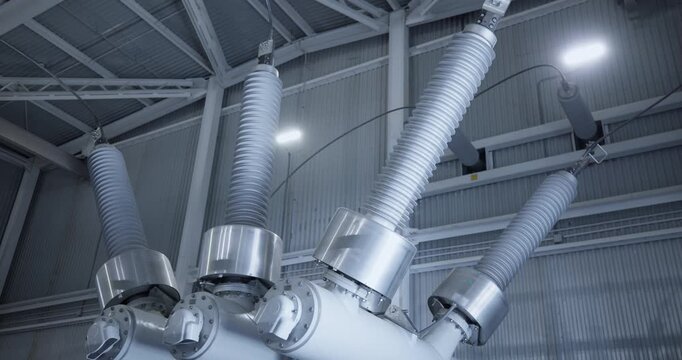 High voltage insulators tilting inside industrial electrical substation interior with upward pan.