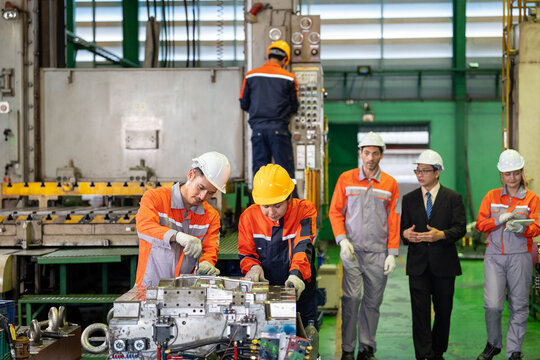 Engineer factory worker machine helmet safety industrial inspection team in orange uniform repairing equipment on workshop floor