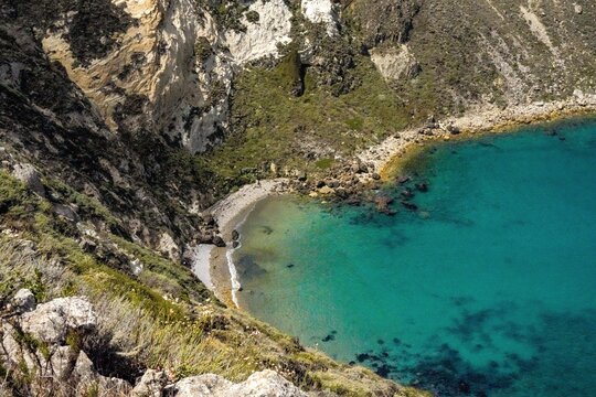 Secluded crescent pebble beach and emerald green water of a sheltered cove seen from the bluff top on Santa Cruz Island in Channel Islands National Park, California