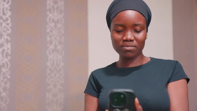 Black mother smiling at phone screen laughing, casual home setting with warm tones and patterned wall, candid video call energy as she reacts to childs messages, playful maternal bond, vibrant joyful