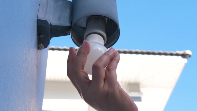 Close up shot of a person hand replacing or installing an energy-saving LED light bulb into an outdoor wall lamp fixture of a residential building