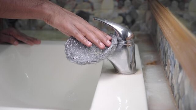 Cleaning a faucet with a metal scrubber in the bathroom