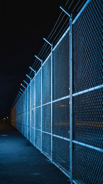 A tall chain-link fence illuminated by blue lights at night.