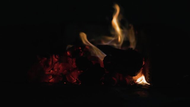 macro video shot of glowing red hot charcoal embers and slowly dying yellow flames burning out inside a dark brick fire pit isolated against a pitch black background for dramatic overlay effects