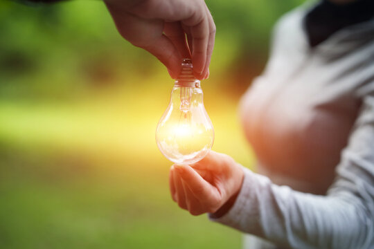 Hand Passing Glowing Light Bulb for Sharing Ideas and Clean Energy Concept