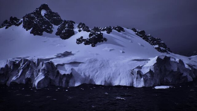 Dusk Antarctic coastline with jagged glacier, cliffs plunging into dark sea, low light overcast sky, brooding atmosphere and climate change undertones