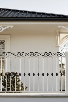 Wrought iron porch railing detail with white paint and decorative elements, showcasing upscale design against a light-colored house exterior