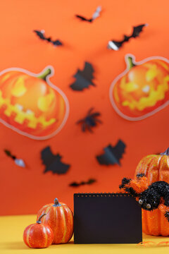 Halloween event template with blank notebook, decorative pumpkins, paper bats, and spider on orange background