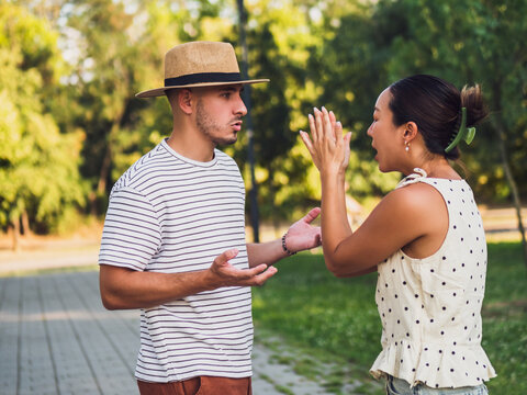 Young man and woman arguing outdoors, showing strong emotions and expressive body language during a disagreement.