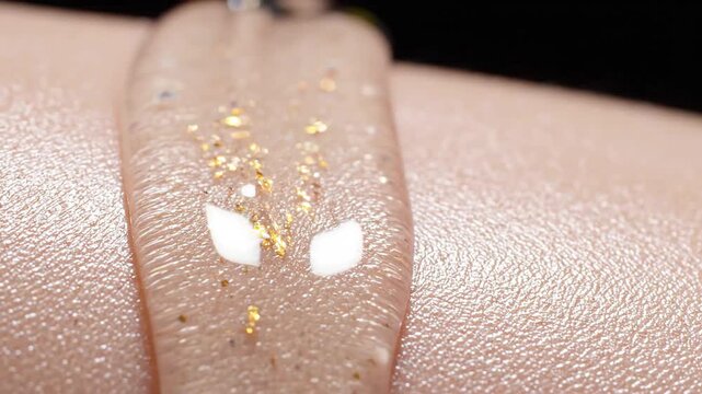 Macro close up of a luxurious transparent gel serum infused with sparkling gold flakes being applied on human skin surface for premium skincare and beauty treatment video