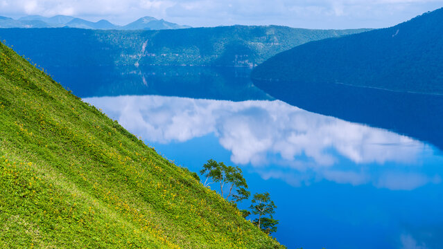 Green volcanic slope and deep blue Lake Mashu under summer clouds
