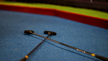 Two Crossed Miniature Golf Putters on a Blue Artificial Turf Course © blueringmedia