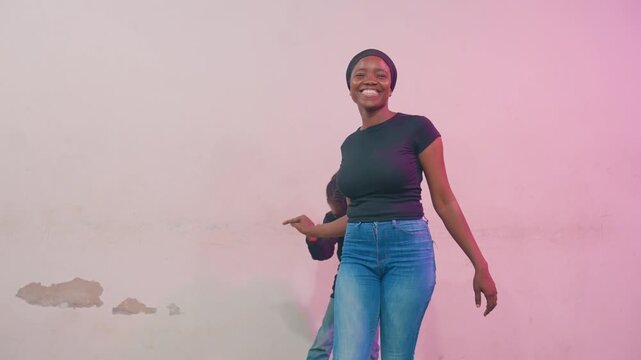 Carefree black mother dancing with child. Pink wall backdrop, casual jeans, walking and playful steps, mentor vibe, guiding movement, rhythmic connection, laughter and confidence in urban studio