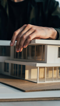 Person's hand touching architectural model of a modern building.