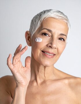 Retrato en primer plano de una mujer senior con una piel facial envejecida pero saludable d&aacute;ndose crema rejuvenecedora sobre la piel