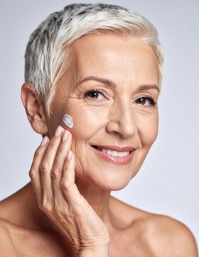 Retrato en primer plano de una mujer senior con una piel facial envejecida pero saludable d&aacute;ndose crema rejuvenecedora sobre la piel