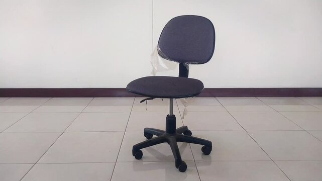 Empty black swivel office chair sliding or rolling smoothly into the center of the frame against a clean white wall and tiled floor