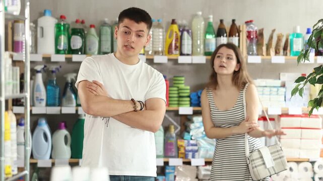 Young woman stands in a supermarket upset and resentful of a man who is standing in the background and talking emotionally. Couple quarrels in the hardware store