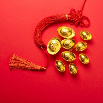 Traditional Chinese gold ingots and a red knot tassel symbolizing prosperity on a vibrant red background.