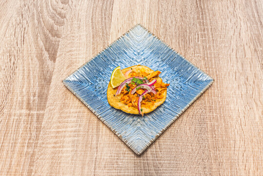 Single tinga taco with red onion and lime wedge centered on a diamond-oriented textured blue plate.