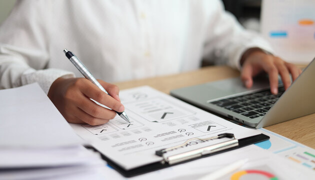Business professional reviewing analytics reports, writing notes, and working on a laptop at a desk, representing data analysis, strategic planning, productivity, research, and digital workflow.